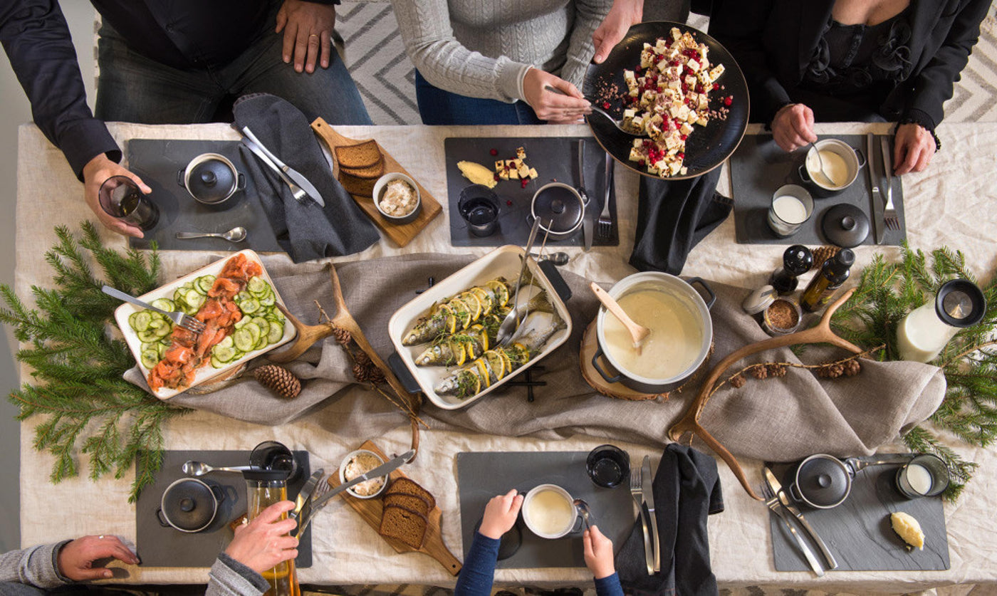 Festlig dukning med produkter från Maku Kitchen Life – serveringsfat med lax och gurka, ugnsbakad fisk med citron, fonduegryta och eleganta köksredskap på en rustik bordsmiljö.